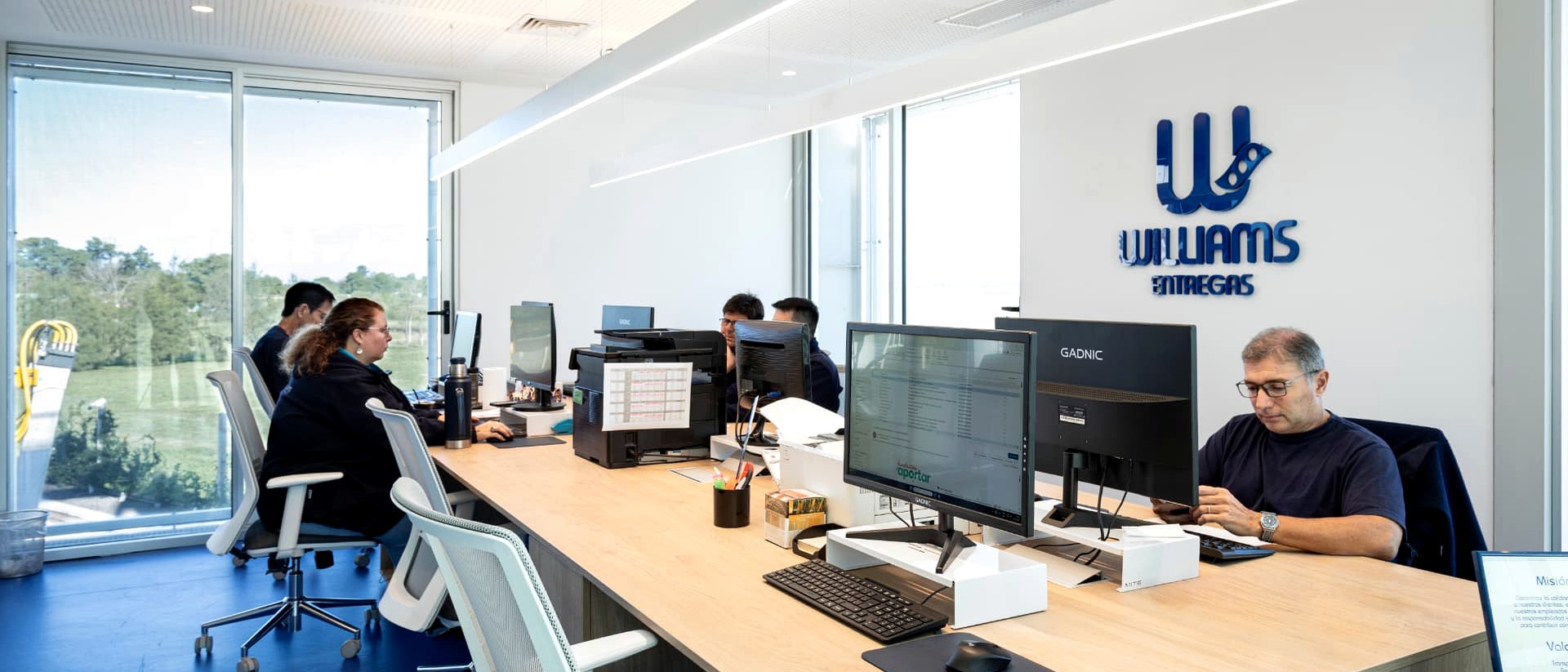Williams Entregas team working at the operations desk in the San Lorenzo office, with the vertical's logo on the wall.